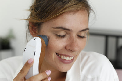 Woman using a handheld RF device on her face, smiling.